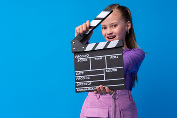 Smiling girl holding clapper board against blue background