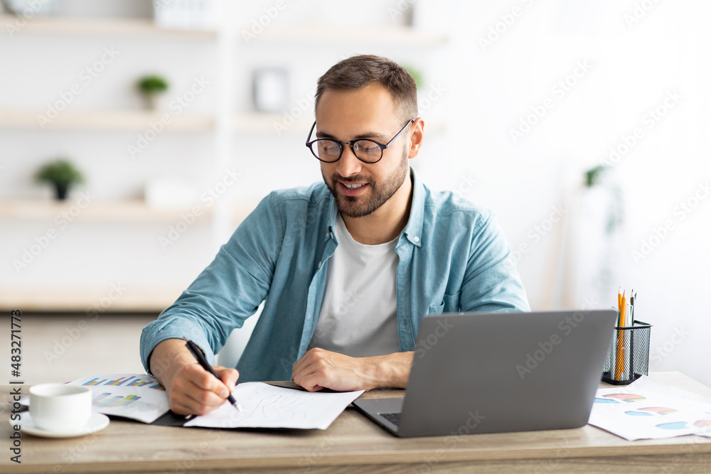 Aufkleber young caucasian businessman taking notes while working on laptop computer at home office