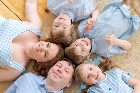 Happy family concept. Top view happy family five tied to each other and smiling, lying on a wooden floor with a carpet. Caucasian large family in the living room on a warm floor