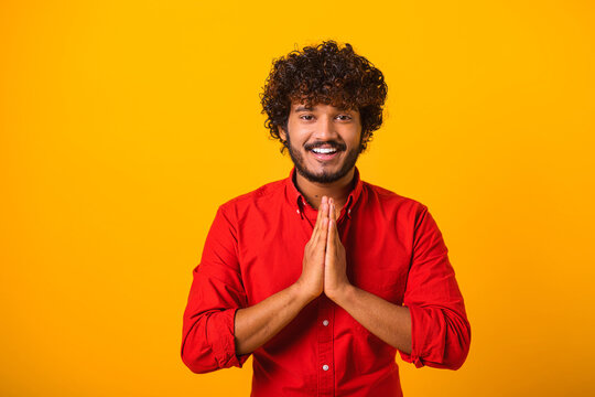 Young bearded man folding hands in prayer, closing eyes and talking to god, asking for help, expressing gratitude. Indoor studio shot isolated on orange background