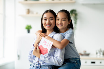 Pretty asian girl greeting mom with Mother's day, daughter with handmade gift card embracing her...