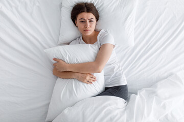 Unhappy sad upset european young woman hugging pillow, suffering from pain and loneliness, lying on...