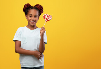 Pretty black girl holding candy, yellow studio background