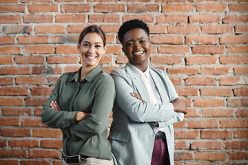Fototapeta na wymiar Confident Caucasian businesswoman and her African American female colleague stand with arms crossed and looking at camera.