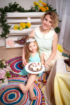 Nice mom and beautiful blonde daughter in room durin spring photo shoot before easter with festive decorated eggs. Happy girl and woman having rest and joy together