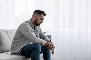 Unhappy young european man sit in living room interior, think about problems