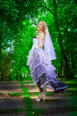 Portrait of beautiful pretty bride in an unusual wedding dress walking and standing alone in the green park in a summer or spring day