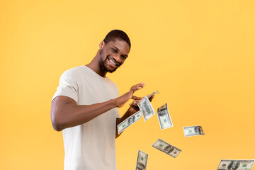 Big win, cashback, wealth concept. Young african american guy throwing out money bills, yellow...