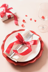 Valentines day table setting with gift, red roses, hearts on pink background. Valentine's invitation to dinner. Vertical format.
