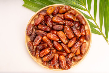 Dried date palm fruit on a wooden plate, date palm fruit with leaf on wooden background