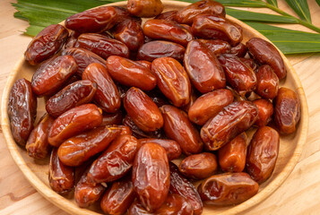 Dried date palm fruit on a wooden plate, date palm fruit with leaf on wooden background