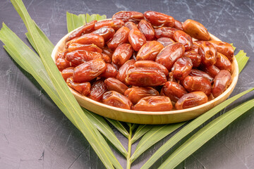 Dried date palm fruit on a wooden plate, date palm fruit with leaf on wooden background