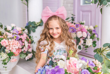 Portrait of a little smiling girl in the studio. A doll girl with a big bow on her head and cute curls..