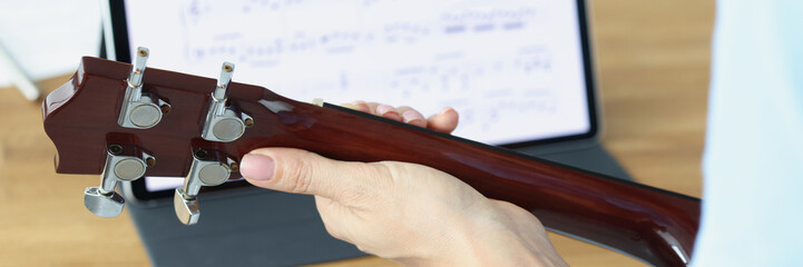 Guitar in female hands on background of tablet with musical notes closeup