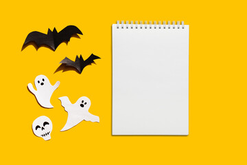 Halloween set decorations with ghost, bat and mock up notebook list on yellow background. Holiday party, minimal card, spooky concept. flat lay, copy space, top view, place for text