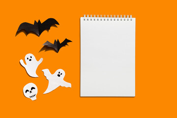 Halloween set decorations with ghost, bat and mock up notebook list on orange background. Holiday party, minimal card, spooky concept. flat lay, copy space, top view