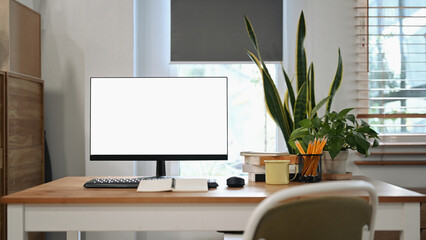 Fototapeta premium Front view computer, coffee cup, pencil holder and house plant on wooden table at home office.