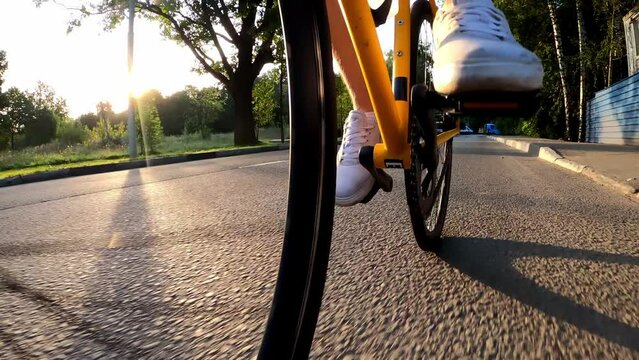 Legs of a cyclist quickly pedaling a bicycle that rides on the road in summer