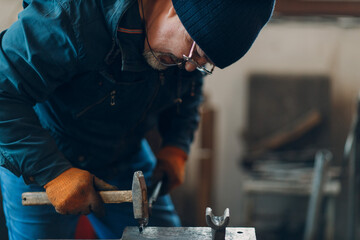 Blacksmith forges and making arrow metal detail with hammer and anvil at forge.