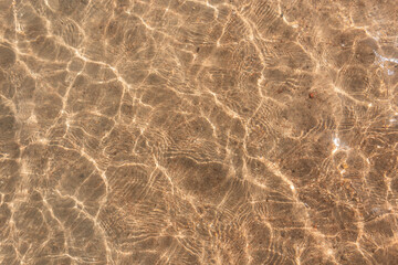 Fototapeta na wymiar Beautiful clear water with light reflections and waves over yellow sandy beach, top view. Abstract water texture. Summer vacation on the red sea