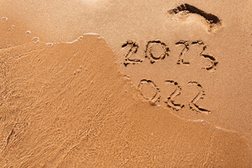 Goodbye 2022 Happy New Year 2023 lettering on beach with wave and clear sea on sunny day. Handwritten inscription 2022 and 2023 on beautiful golden sand beach. New Years 2023 replace 2022 concept