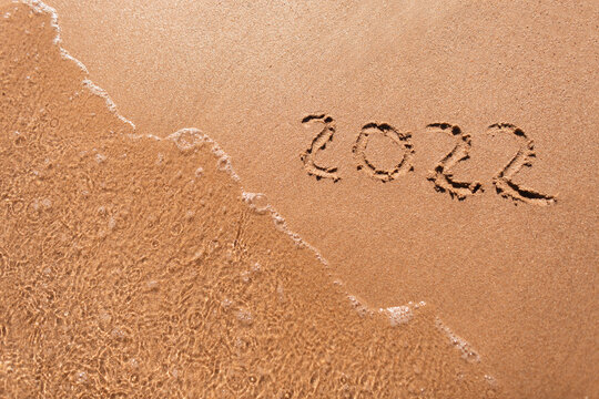 2022 is drawing on yellow sand on a beach with a wave by the sea. Summer vacation concept, concept. New Year's Eve and an inscription on the sand