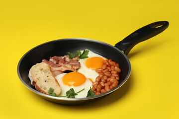 Pan with tasty breakfast on yellow background