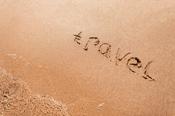 Travel text written on the sand of a beach by the sea. Summer holidays and travel concept, top view