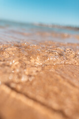 Beautiful sea water on yellow beach sand with blue sky, close-up. Macro water. Summer rest and vacation