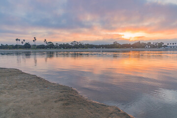 Sunrise on the Mission Bay in California shows boats with their reflections in the orange of the rising sun. Sailors ready to take their sailboats on an adventure