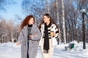 Two cheerful girlfriends are walking in the winter park