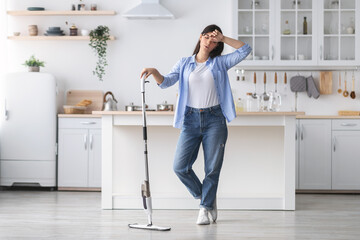 Tired woman cleaning floor with mop in kitchen