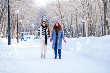 Fototapeta na wymiar Two cheerful girlfriends are walking in the winter park