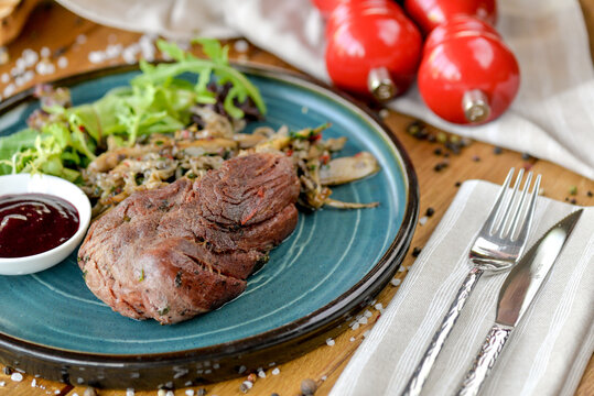 Big Steak On A Blue Plate With Herbs And Sauce In A Gravy Boat Macro Photo
