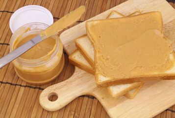 Peanut butter spread, table knife and bread slices on cutting board.