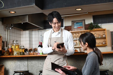 カフェ（飲食店）で働く配膳中のアジア人の男性の店員と女性客