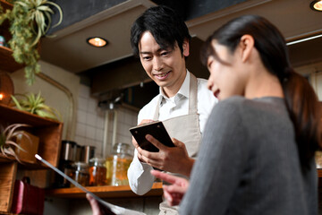 カフェ（飲食店）で働く配膳中のアジア人の男性の店員と女性客