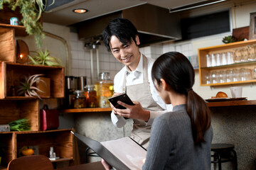 カフェ（飲食店）で働く配膳中のアジア人の男性の店員と女性客