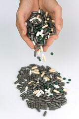 Many black and white pills falling from a man's hand into a pile below, bunch of pharmaceutical medicine or supplements