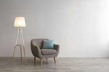 Retro armchair with blue pillow, glowing lamp on floor on gray wall background in office or living room