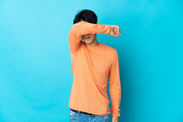 Young Chinese man isolated on blue background covering eyes by hands