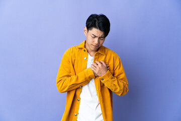 Young Chinese man isolated on purple background having a pain in the heart