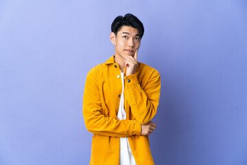 Young Chinese man isolated on purple background and thinking