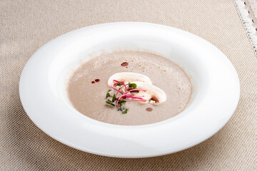 Cream-soup of mushrooms with microgreens on a white plate.