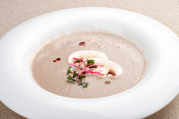 Cream-soup of mushrooms with microgreens on a white plate.