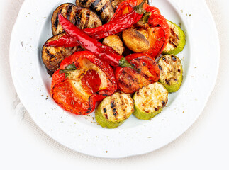 Grilled roasted vegetables on a white plate.  Sweet peppers, tomatoes, zucchini, eggplant. Top view