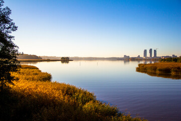Fototapeta premium Calm sunny autumn morning with city skyline reflected in water