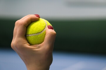 Close-up of tennis ball in woman`s hand with red nails. Blue tennis court n background.