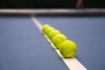 Row of tennis balls on white line on blue hard tennis court.