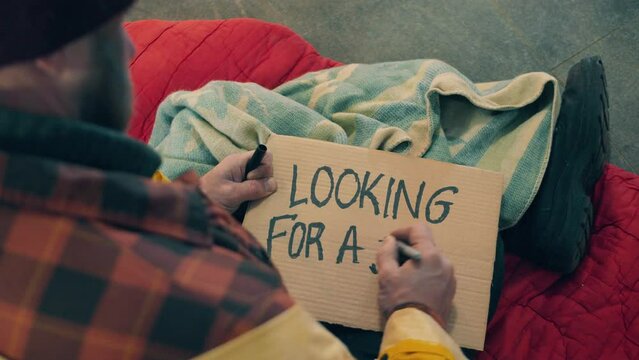 A beggar is writing 'looking for a job' on a plate